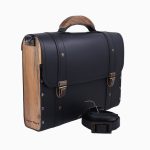 Sac à main Frankie, avec une structure en cuir noir et des panneaux en bois sur les côtés. Il présente des fermetures dorées et une poignée supérieure, accompagné d'une bandoulière assortie.