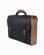 Sac à main Frankie vu de profil, avec une finition en cuir noir et des panneaux en bois sur le côté. Le sac présente des fermetures dorées et une poignée en bois, soulignant son design élégant.